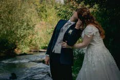 Brautpaar küsst sich in der Natur mit einem Bach im Hintergrund