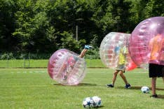 Mehrere Teilnehmer beim Bubble Soccer mit mehreren Fussbällen im Freien