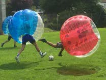Bubble Soccer Spieler im Zweikampf mit einem Fussball beim Rennen