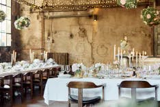 Weiss gedeckte und dekorierte Tische mit brennenden Kerzen für ein Hochzeitsessen