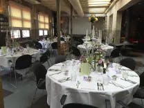Raum mit mehreren runden Tischen die alle in weiss gedeckt sind für ein Abendessen bei einem Hochzeit
