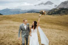 Brautpaar lacht und hält Blumenstrauss in die Höhe