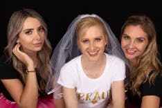 Braut mit Schleier posiert mit zwei Freundinnen beim Junggesellenabschied